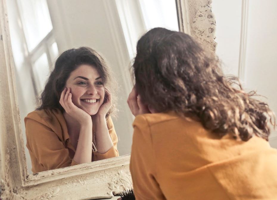 Photo of woman cheerily smiling into the mirror.