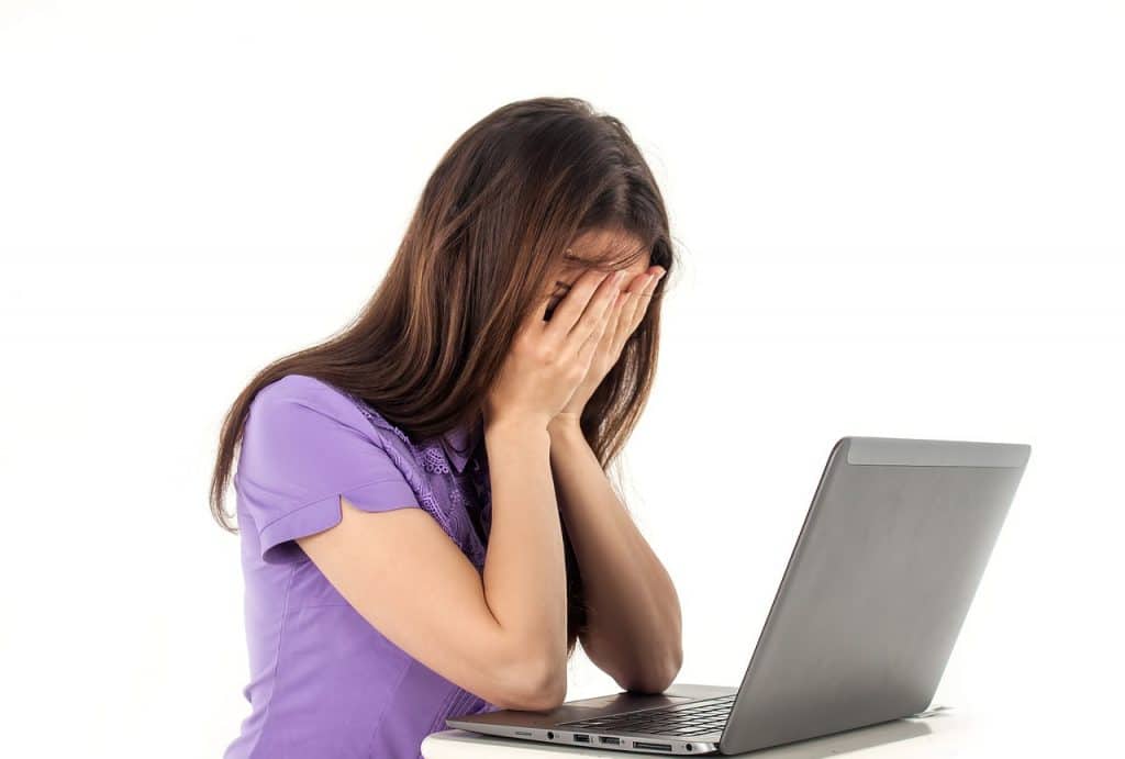 a girl covering her face like she's crying in front of a laptop