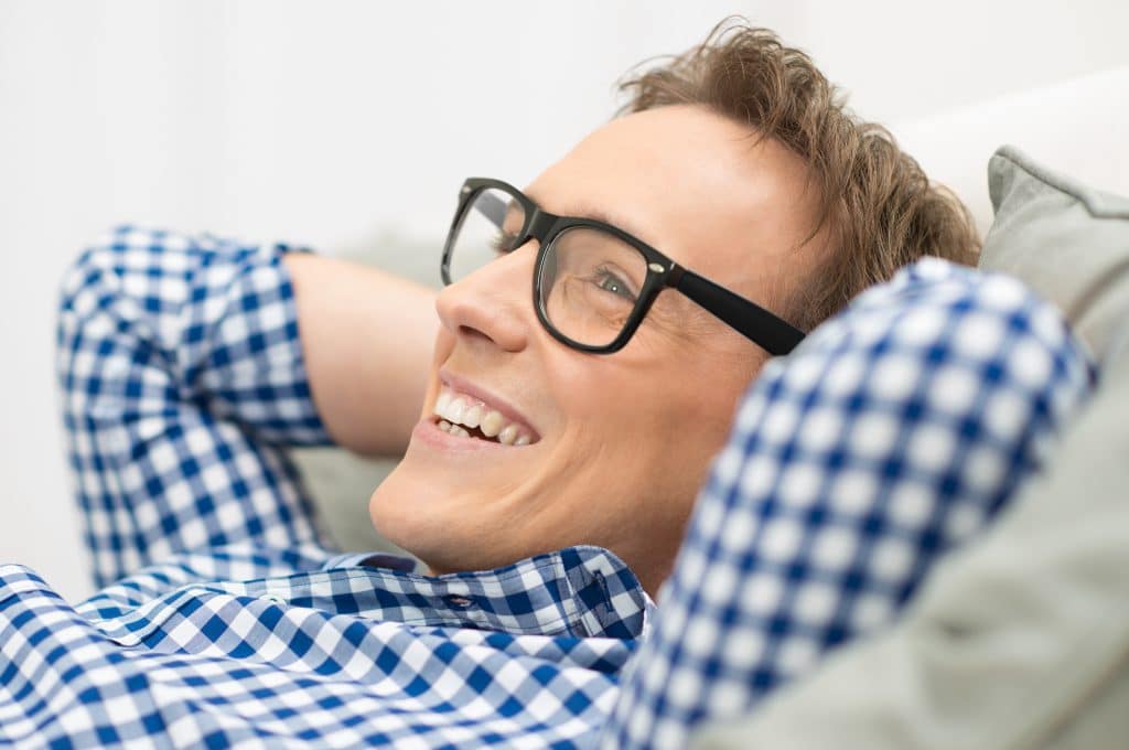 a happy man wearing glasses and relaxing on a couch